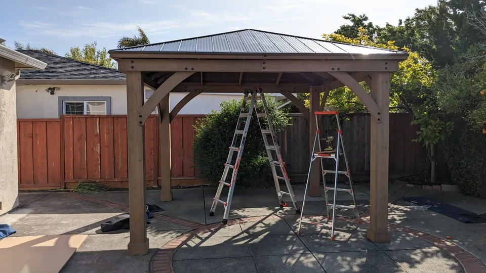 A roofed gazebo assembly on a paved patio.