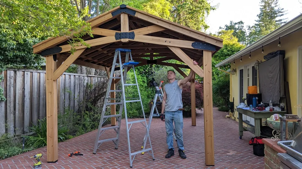 Artem beneath the timber frame of a gazebo during assembly